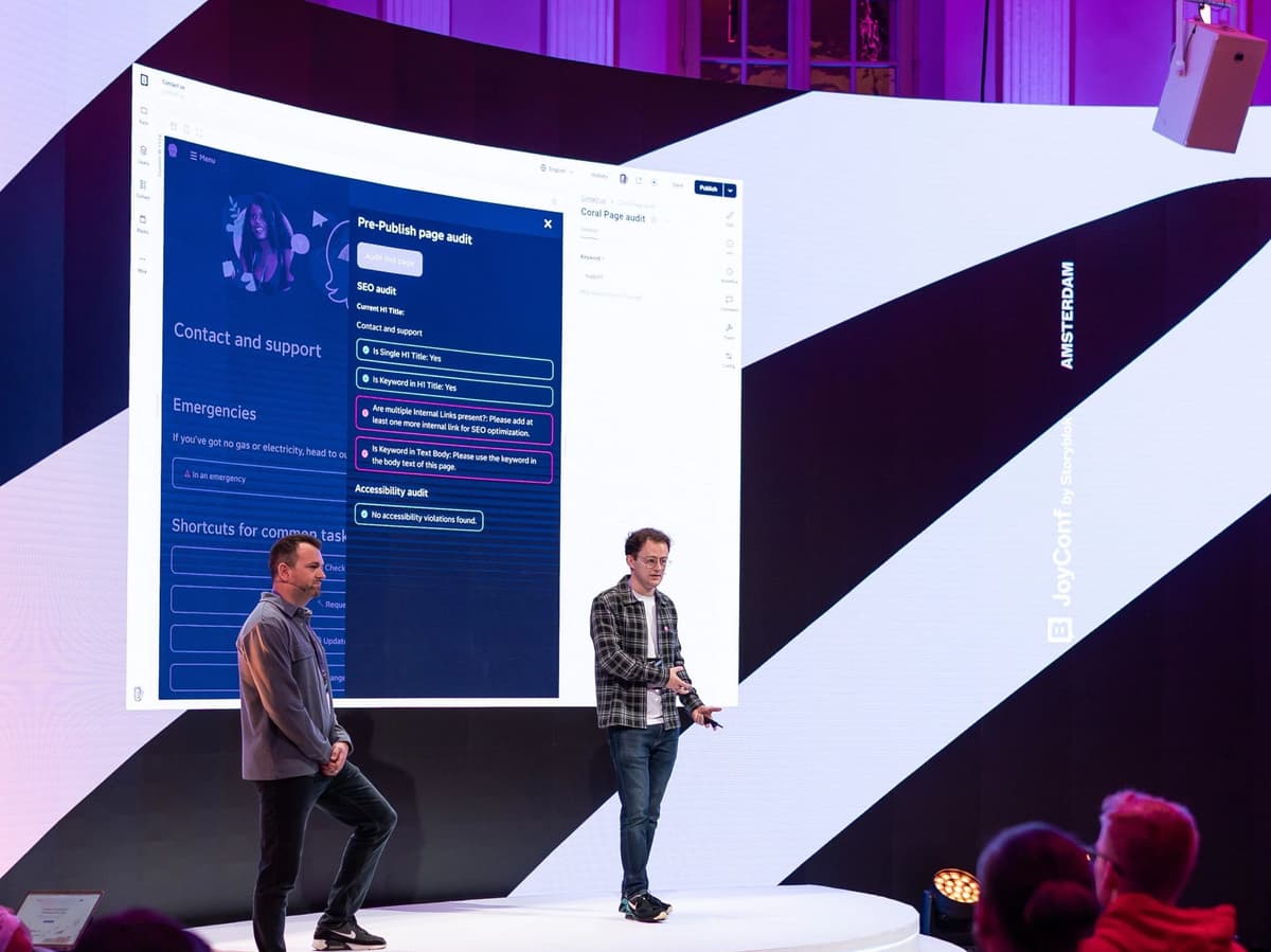 Aaron stood on a stage alongside Alex Brown, in front of a large screen showing user interface screenshots